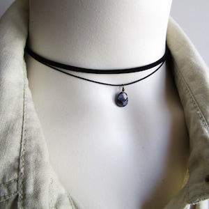 May include: A black choker necklace with a small, dark blue gemstone pendant.