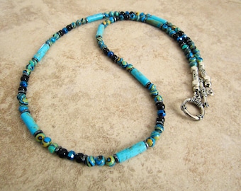 May include: A turquoise and black beaded necklace with a silver clasp. The necklace features cylindrical turquoise beads interspersed with smaller black and blue beads. The clasp is a decorative silver ring.