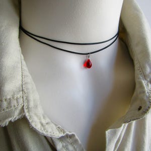 May include: A black choker necklace with a small red teardrop pendant.