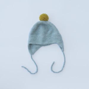 May include: A light blue knitted baby hat with a yellow pom-pom on top and two long ties.
