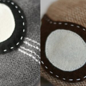 May include: Two close-up images of knitted fabric with a circular patch sewn on. The patch on the left is black with white stitching and a white circle in the center. The patch on the right is brown with white stitching and a white circle in the center.
