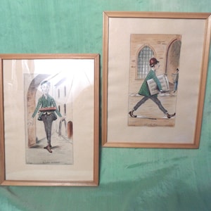 May include: Two framed watercolor prints. One shows a person in a green jacket and dark pants carrying a tray of items. The other depicts a person in a green jacket and dark pants walking with a stack of papers. Both are set in a European town.