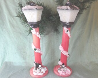 May include: Two vintage Christmas candle holders shaped like streetlights with pink and white candles and a snowman at the base.