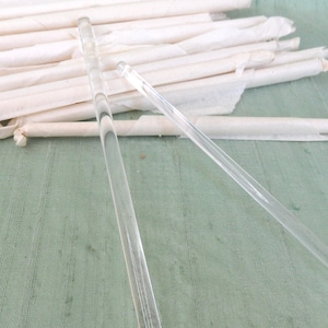 May include: Two clear glass rods, one longer than the other, lying on a green fabric surface. The rods are thin and cylindrical.