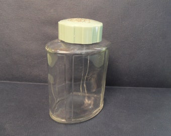 May include: A clear glass bottle with a green plastic lid. The bottle has a rounded rectangular shape and is empty.