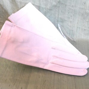Könnte beinhalten: Ein Paar rosa Lederhandschuhe. Die Handschuhe sind in der Mitte gefaltet und die Fingerspitzen sind sichtbar.