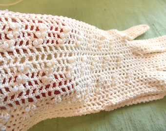 May include: A pair of white crocheted gloves with pearl-like beads throughout the fabric.