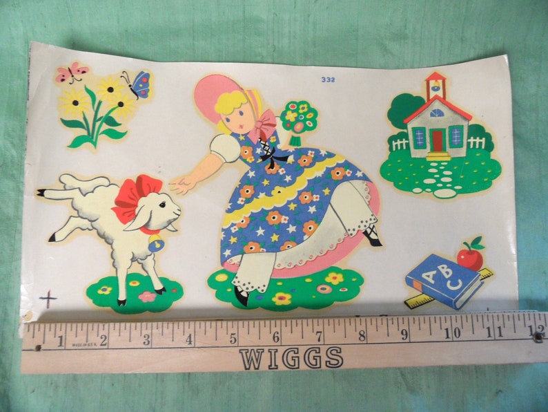 May include: A vintage children's illustration featuring a girl in a blue and yellow dress with a pink hat, a white lamb with a red bow, a small schoolhouse, and an ABC book with a red apple. The illustration is printed on a white background.