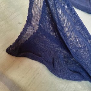 May include: Close-up of a navy blue mesh fabric with a scalloped edge. The fabric is draped over a light gray surface, creating shadows and texture. The mesh has a fine, open weave.
