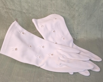 May include: A pair of white gloves featuring a series of small, circular cutouts arranged in a scattered pattern across the fabric. The gloves extend past the wrist and are constructed from a smooth, opaque material with stitched finger details.