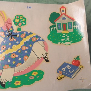 May include: A vintage sticker sheet featuring a girl in a blue and white dress, a schoolhouse, and an ABC book with a red apple on top. The sticker sheet is on a white background.
