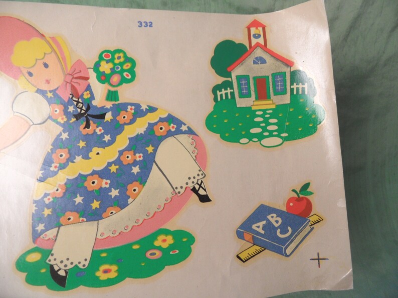 May include: A vintage sticker sheet featuring a girl in a blue and white dress, a schoolhouse, and an ABC book with a red apple on top. The sticker sheet is on a white background.