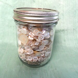 May include: A glass jar filled with a variety of white and off-white buttons.