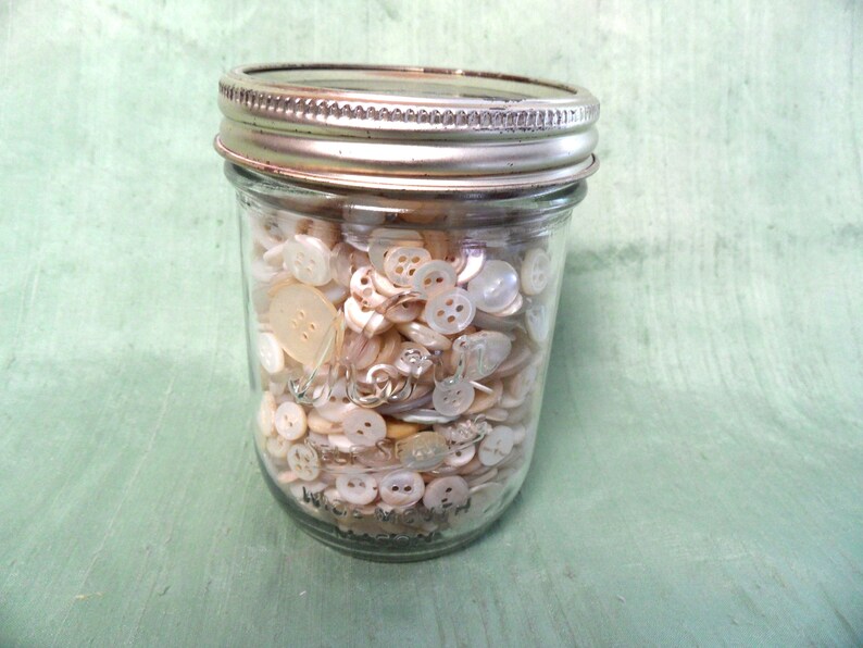 May include: A glass jar filled with a variety of white and off-white buttons.