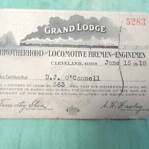 May include: A vintage Brotherhood of Locomotive Firemen and Enginemen membership card dated 15 June 1918. The card is printed on cream paper with black text and features a black and white illustration of a train. The card number is 5283 and the member's name is D.J. O'Connell. The card certifies that the member is protected during the war.