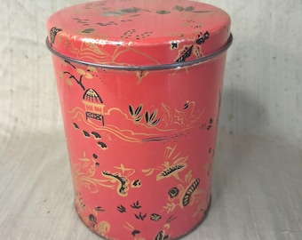 May include: A cylindrical red metal storage tin featuring a repeating black and gold print of pagodas, stylized trees, and floral motifs. The container includes a matching circular lid that fits securely over the top rim of the vessel.