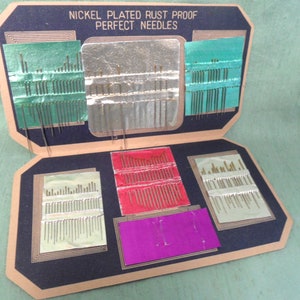 May include: A vintage cardboard box containing a collection of nickel-plated rust-proof sewing needles. The needles are organized in rows and are held in place by a green, silver, and red backing. The box has a black background and the text "Nickel Plated Rust Proof Perfect Needles" is printed on the front.
