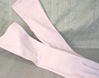 May include: A pair of long, pale pink opera-length gloves made of a smooth, opaque fabric. The gloves extend well past the wrist, featuring a simple, clean design with stitched seams along the fingers and a straight opening at the forearm.