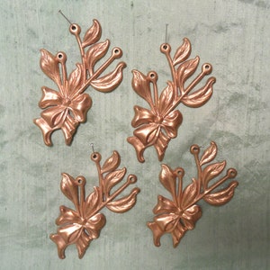 以下が含まれることがあります： 銅仕上げのアンティーク調金属製フラワーエンベリッシュメント4点。各ピースにはリボンと葉が施されています。