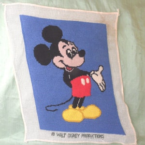 May include: A blue and white needlepoint canvas with a cartoon image of Mickey Mouse. Mickey is wearing red shorts and yellow shoes. The canvas has the text "© WALT DISNEY PRODUCTIONS" at the bottom.