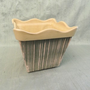 Puede incluir: Un macetero cuadrado de cerámica con un borde ondulado y un diseño texturizado a rayas en tonos verdes y rosas.