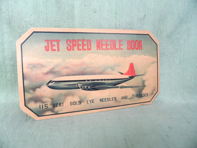 May include: Vintage cardboard needle book with a red and white airplane flying through clouds. The text on the book reads "Jet Speed Needle Book 115 Best Gold Eye Needles and Threader".
