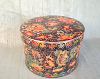May include: A round metal container with a lid, featuring a dark brown background decorated with a vibrant floral pattern in shades of orange, red, yellow, and green. The design includes intricate, swirling line work throughout.