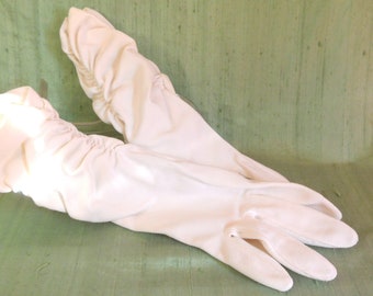 May include: A pair of white satin gloves with a gathered cuff. The gloves are lying on a green surface.