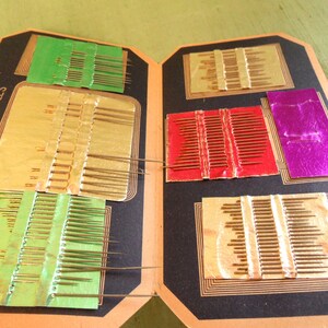 May include: A vintage sewing needle case with a black cover and gold lettering that reads "Nickel Plated Rust Proof Perfect Needles". The case has multiple compartments with rows of needles in different sizes and colors.