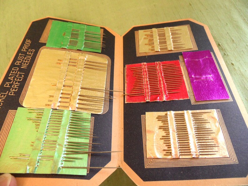 May include: A vintage sewing needle case with a black cover and gold lettering that reads "Nickel Plated Rust Proof Perfect Needles". The case has multiple compartments with rows of needles in different sizes and colors.