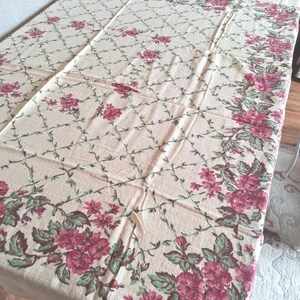 May include: A rectangular tablecloth featuring a cream-coloured base with a repeating green lattice pattern. The fabric is decorated with clusters of deep pink roses and green leaves arranged in a border along the edges and across the surface.