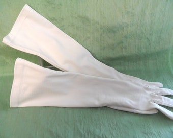 May include: A pair of long white gloves made of a soft, stretchy fabric. The gloves are folded in half and laid out on a green surface.