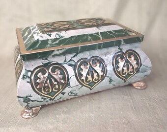 May include: A rectangular box with a green and white faux marble finish, featuring metallic gold-toned accents. The lid and sides are decorated with ornate, heart-shaped filigree patterns. The box is supported by four small, metallic gold-toned feet.