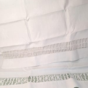Puede incluir: Una pieza textil blanca con una textura de tela tejida y un sutil patrón de estrellas. La sección inferior muestra una banda horizontal de detalles calados verticales seguida de un borde de encaje con un intrincado motivo floral.
