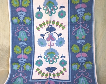 May include: A rectangular textile runner featuring a central pale pink panel flanked by two dark blue vertical borders. The fabric displays a repeating floral pattern in shades of light blue, lime green, and purple, arranged in symmetrical vertical vines.