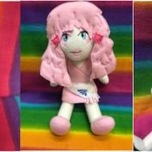 May include: Three handmade plush dolls with anime-inspired features. The dolls have colorful hair, detailed facial features, and unique outfits. The background is a vibrant rainbow pattern, enhancing the dolls' colorful appearance.