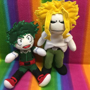 May include: Two plush dolls of anime characters. One doll has green hair, a green and red outfit, and red shoes. The other doll has yellow hair, a white shirt, green pants, and black shoes. The dolls are on a rainbow-colored background.