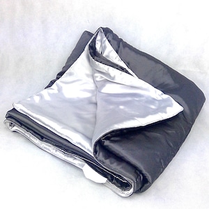 May include: A soft, reversible blanket with a black side and a silver side. The blanket is folded in half, showing both sides.