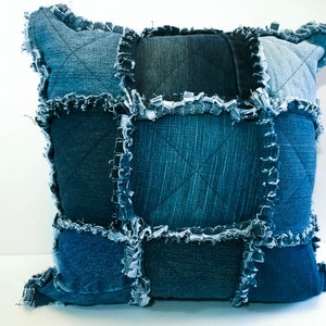May include: A blue denim pillow with a patchwork design. The pillow is made from different shades of blue denim and has a frayed edge.