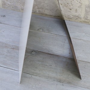 May include: A white card with a silver edge is standing upright on a light wood surface.