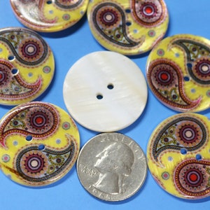 May include: Assortment of colorful buttons with a paisley design. The buttons are yellow with red, pink, and blue accents. There is also a plain white button with two holes.