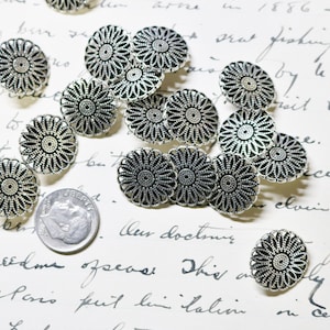 May include: Silver-toned metal floral buttons with a detailed, openwork design. The buttons are arranged on a vintage paper background, with a dime for size comparison. The buttons have a scalloped edge and a central, textured pattern.