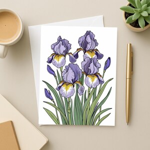 May include: Greeting card featuring a detailed illustration of purple iris flowers with yellow and white accents. The flowers are set against a white background with green leaves. A gold pen and a cup of coffee are also visible.