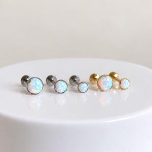 May include: A collection of five stud earrings featuring round, iridescent white opal cabochons. Three studs have silver-toned metal posts and settings, while two studs feature gold-toned metal posts and settings. Each earring has a flat back post.