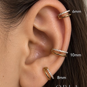 May include: Three gold-toned double-band ear cuffs, each featuring one plain band and one band set with clear stones. The cuffs are labeled with sizes 6mm, 8mm, and 10mm. The text ORLA STUDIO is visible in the bottom right corner of the image.