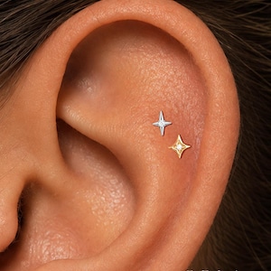 Pode incluir: Dois brincos em forma de estrela, um prateado e outro dourado, cada um com uma pequena pedra central. O texto Mix Silver and Gold e ORLA STUDIO é visível na parte inferior da imagem.