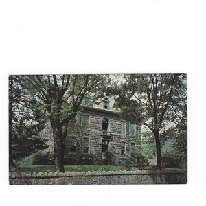 Puede incluir: Una postal vintage que muestra un gran edificio de piedra con varias ventanas y un porche. Los árboles enmarcan el edificio, que se encuentra detrás de un muro de piedra. La postal tiene una apariencia ligeramente descolorida.