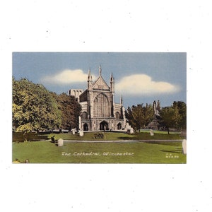 May include: Vintage postcard featuring The Cathedral, Winchester. The image shows a large cathedral with intricate architectural details, set against a backdrop of green grass and trees. The sky is blue with fluffy white clouds. The text "The Cathedral, Winchester" is visible.