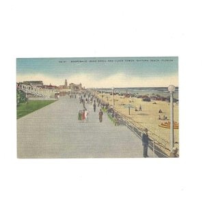 May include: Vintage postcard featuring the Daytona Beach boardwalk with people strolling along the paved path. The text reads "Boardwalk, Sand Shell and Clock Tower, Daytona Beach, Florida."