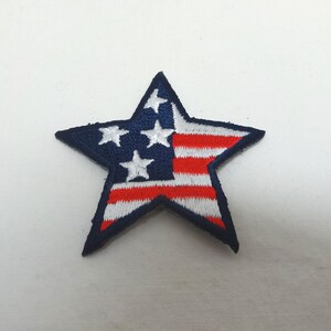 Pode incluir: Um remendo azul em forma de estrela com um design de bandeira americana vermelha, branca e azul.